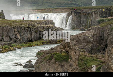 Persone che guardano l'acqua che sgorga dalla cascata di Goðafoss. Godafoss si trova nel nord dell'Islanda a circa 45 minuti da Akureyri, la seconda large dell'Islanda... Foto Stock