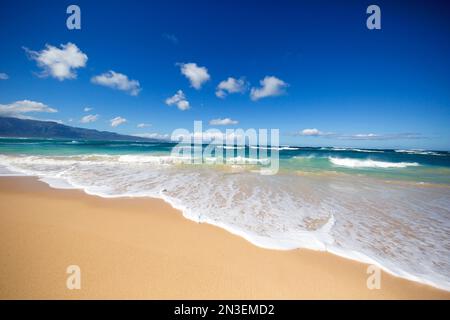 Acque turchesi con il surf che lambisce la riva e un cielo azzurro luminoso a Baldwin Beach, sulla costa nord di Maui Foto Stock