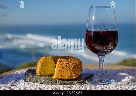 Abbinamento di cibo e bevande portoghesi, bicchiere di vino porto bruno e coccodrillo pastais de bacalhau, servito all'aperto con vista sul blu soleggiato Atla Foto Stock