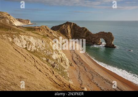Gente che cammina lungo la spiaggia con vista sull'Oceano Atlantico e sulla formazione rocciosa Durdle Door sulla Jurassic Coast vicino a Lulworth Foto Stock