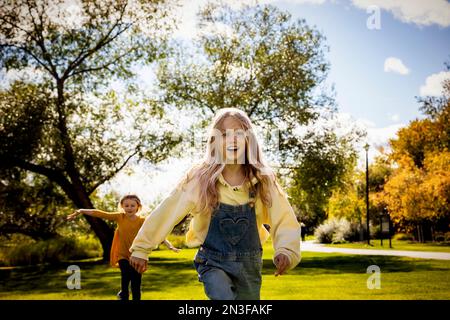 Due sorelle si divertono a vicenda e giocano insieme mentre corrono sull'erba in una calda giornata autunnale in un parco cittadino Foto Stock