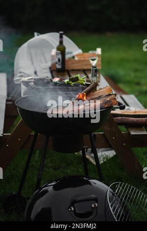 Il braciere fumante di una forma rotonda. La legna da ardere si accende nel braciere sullo sfondo di un tavolo e sedie. Il concetto di pic-nic, relax Foto Stock