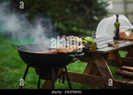 Il braciere fumante di una forma rotonda. La legna da ardere si accende nel braciere sullo sfondo di un tavolo e sedie. Il concetto di pic-nic, relax Foto Stock