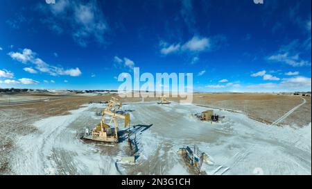 Vista aerea delle pompe in un campo innevato con cielo blu, nuvole e montagne innevate in lontananza, a ovest di Airdrie, Alberta Foto Stock