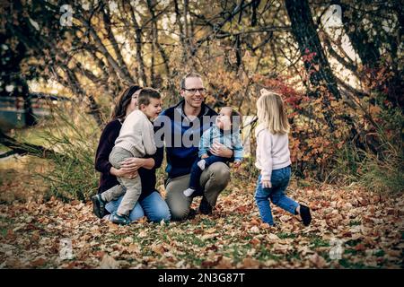 Famiglia giovane con tre bambini, figlia più giovane con sindrome di Down, che si diverte insieme in un parco cittadino durante la stagione autunnale Foto Stock