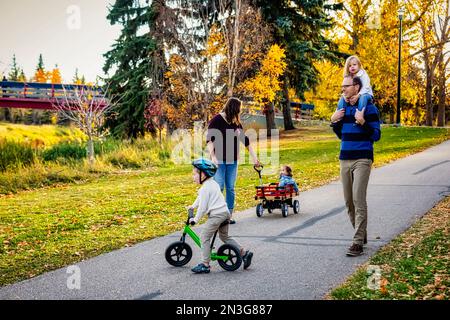 Una madre che tira la figlia con la sindrome di Down in un carro, il padre ha la figlia sulle spalle e il figlio sta cavalcando la sua bicicletta in una... Foto Stock