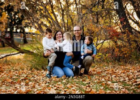 Ritratto di una giovane famiglia con tre figli, figlia più giovane con sindrome di Down, in un parco cittadino durante la stagione autunnale Foto Stock