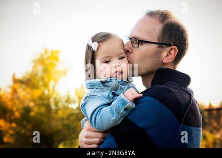 Il padre tiene e bacia la figlia che ha la sindrome di Down in un parco durante la stagione autunnale; St. Albert, Alberta, Canada Foto Stock