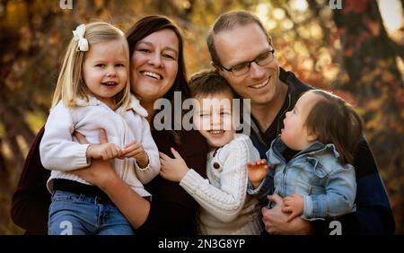 Ritratto di una giovane famiglia con tre figli, figlia più giovane con sindrome di Down, in un parco cittadino durante la stagione autunnale Foto Stock