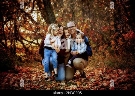 Ritratto di una giovane famiglia con tre figli, figlia più giovane con sindrome di Down, in un parco cittadino durante la stagione autunnale Foto Stock