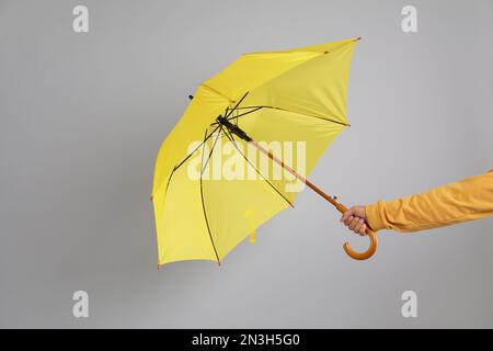 Uomo che tiene l'ombrello catturato in una raffica di vento su sfondo grigio, primo piano Foto Stock