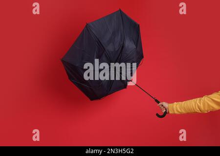 Uomo che tiene l'ombrello catturato in una raffica di vento su sfondo rosso, primo piano Foto Stock