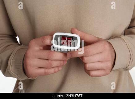 Uomo che utilizza il pulsossimetro per il test del livello di ossigeno su sfondo bianco, primo piano Foto Stock