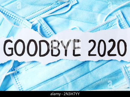 Pezzo di carta con frase Arrivederci 2020 su un mucchio di maschere mediche blu. Concetto di pandemia di coronavirus Foto Stock