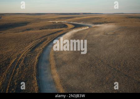 Automobili e camion gettano polvere lungo le strade di ghiaia in una riserva naturale dello stato del Kansas, con bisonti che vagano sulla vasta terra degli Stati Uniti Foto Stock