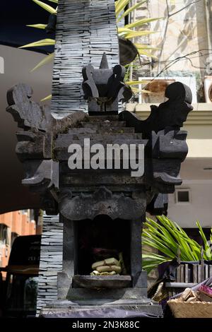 Un canang sari splendidamente organizzato che offre riposi in una tradizionale casa di spirito Balinese, circondato da incenso e fiori Foto Stock