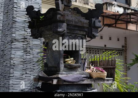 Un canang sari splendidamente organizzato che offre riposi in una tradizionale casa di spirito Balinese, circondato da incenso e fiori Foto Stock