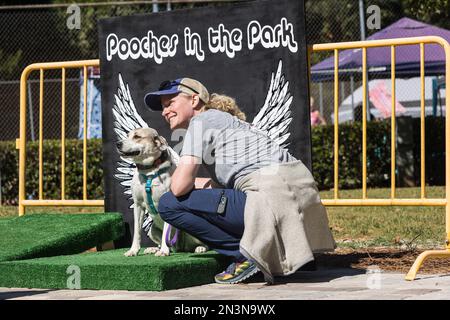 Braselton, GA / USA - 24 settembre 2022: Una donna si inginocchia per scattare una foto con il suo cane seduto contro un angelo ala sfondo foto. Foto Stock