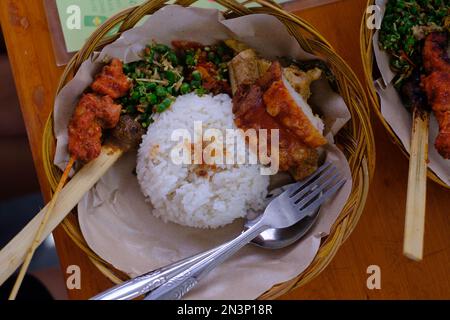 Delizioso maiale succulente servito su un piatto di rattan con riso. Giacitura piatta. Un appetitoso piatto di un succulento suino su un piatto di rattan, circondare Foto Stock