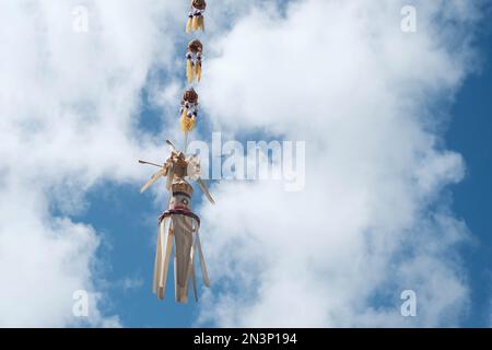 Una tradizionale decorazione Balinese, un Penjor, che oscura nel vento contro un cielo limpido e sfondo nuvoloso Foto Stock