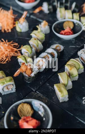 Uno scatto verticale di diversi tipi di sushi rotoli messo sulla scrivania nera su sfondo sfocato Foto Stock