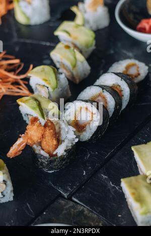 Uno scatto verticale di diversi tipi di sushi rotoli messo sulla scrivania nera su sfondo sfocato Foto Stock