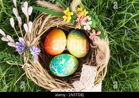 Uova colorate in nido con fiori su erba. Vista dall'alto. Pasqua, Caccia alle uova Foto Stock