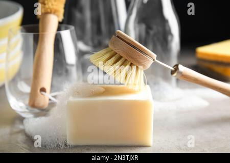 Spazzola per la pulizia e saponetta per il lavaggio delle stoviglie su tavolo grigio, primo piano Foto Stock