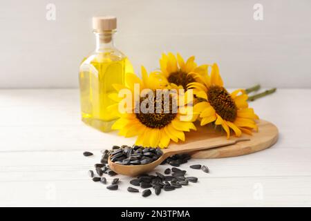 Girasoli, bottiglia di olio e semi su tavola di legno bianco Foto Stock