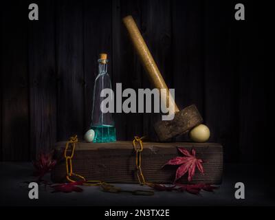 Still Life with Old Hammer, Birds' Eggs, Rusty Chain e bottiglia di vetro su blocco di legno su foglie di acero Foto Stock