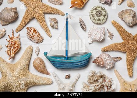 Composizione piatta con nave giocattolo e conchiglie su fondo di legno bianco Foto Stock