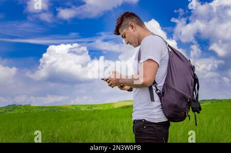 Uomo che chiama dal telefono delle cellule, giovane uomo nel campo che chiama dal telefono delle cellule, giovane zaino in spalla con il telefono delle cellule nel campo e spazio della copia Foto Stock