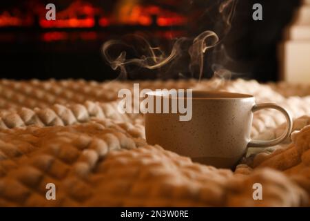 Tazza di bevanda calda su una plaid a maglia vicino al caminetto all'interno. Spazio per il testo Foto Stock