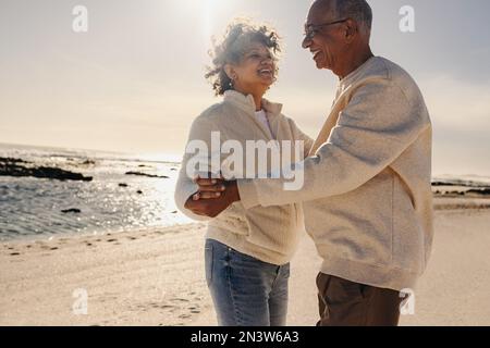 Allegra coppia anziana sorridente mentre ballava insieme in spiaggia. Felice coppia anziana che si trova vicino all'oceano. Coppia matura godendo Foto Stock