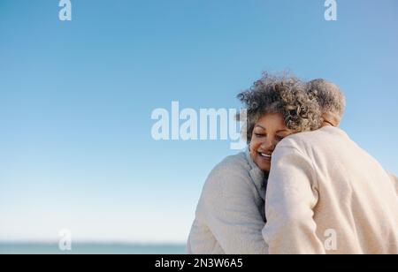 Affettuosa donna anziana sorridente felicemente mentre si appoggia alla spalla del marito in spiaggia. Romantica coppia anziana godendo di un mare rinfrescante Foto Stock