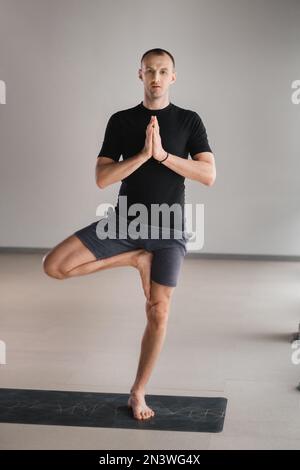Un uomo di costruzione atletica fa yoga in palestra su un tappetino. Foto Stock