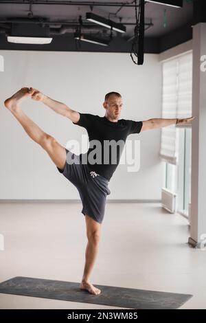 Un uomo di costruzione atletica fa yoga in palestra su un tappetino. Foto Stock