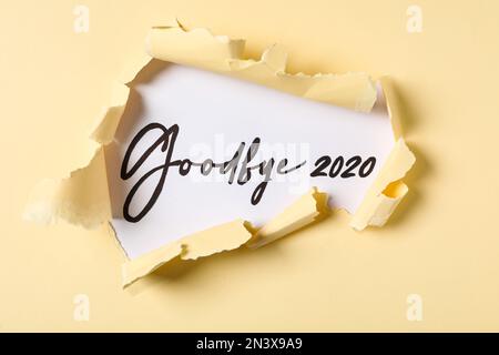 Frase Arrivederci 2020 su sfondo bianco, vista attraverso carta gialla strappata Foto Stock