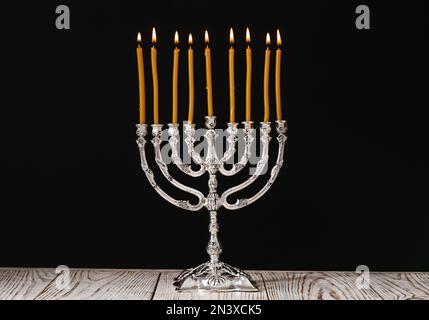 Menorah d'argento con candele accese sul tavolo su sfondo nero. Hanukkah celebrazione Foto Stock