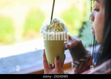 tè verde smoothie tazza di plastica donna mano che tiene una tazza tè verde in caffè, giovane donna che beve latte tè donna rilassata Foto Stock