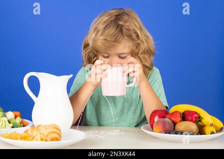 Capretto che versa latte intero di mucche. Ritratto di bambino mangiare cibo fresco sano in cucina a casa. Bambino che mangia la colazione prima della scuola. Foto Stock