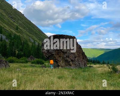 Una ragazza viaggiatrice con uno zaino e un cappello cammina su pali da trekking, sullo sfondo di una grande scogliera di pietra sulle montagne Altai. Foto Stock