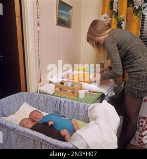 1970s madre. Una donna sta pulendo e cambiando i pannolini sopra delle sue tre babys che si trova su un tavolo cambiante. Ha triplette e due sono visibili nel letto. Svezia 1972 rif BV105-3 Foto Stock