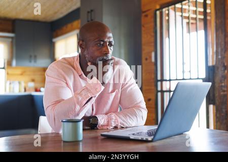 Serio uomo afroamericano calvo anziano con mano sul mento guardando il laptop sul tavolo in cabina di ceppo Foto Stock