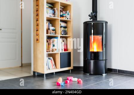 Stufa a pellet con alcuni giocattoli di fronte, con fiamme e biblioteca Foto Stock