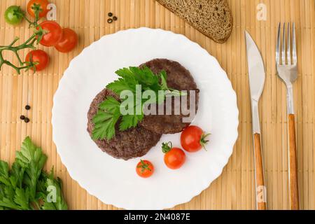 Carne di manzo macinata Burger bistecca cutlet in un piatto bianco su uno sfondo di legno tavola. Cutlet per hamburger con verdure e spezie. fast food Foto Stock