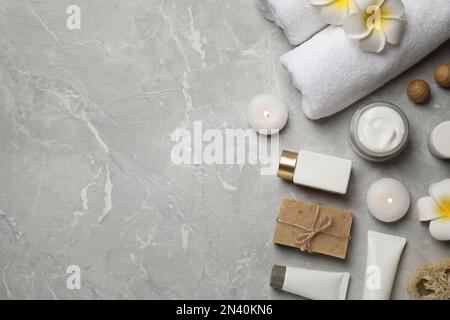 Composizione piatta con asciugamani e prodotti per la cura della pelle su sfondo in marmo grigio chiaro, spazio per testo Foto Stock