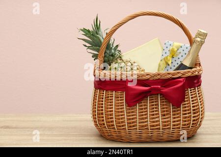 Cestino omaggio in vimini con ananas e bottiglia di champagne su tavolo in legno. Spazio per il testo Foto Stock