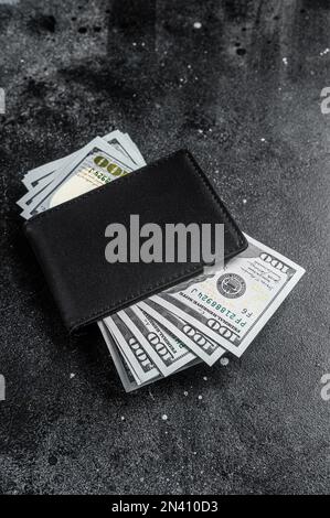 Una borsa nera con il pacchetto grande dei dollari, contanti della nota del dollaro. Sfondo nero. Vista dall'alto. Spazio di copia. Foto Stock