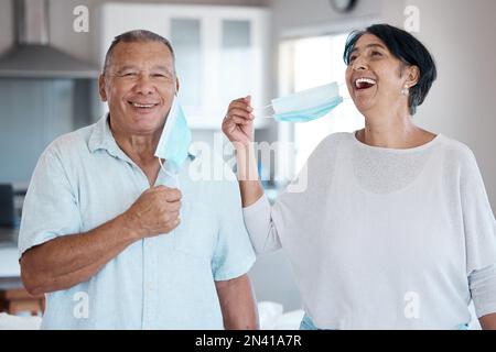 Covid, maschera rimuovere e coppia senior ritratto con un sorriso a casa in cucina. Uomo felice, maturo e matrimonio di un nonno in una casa ridendo Foto Stock